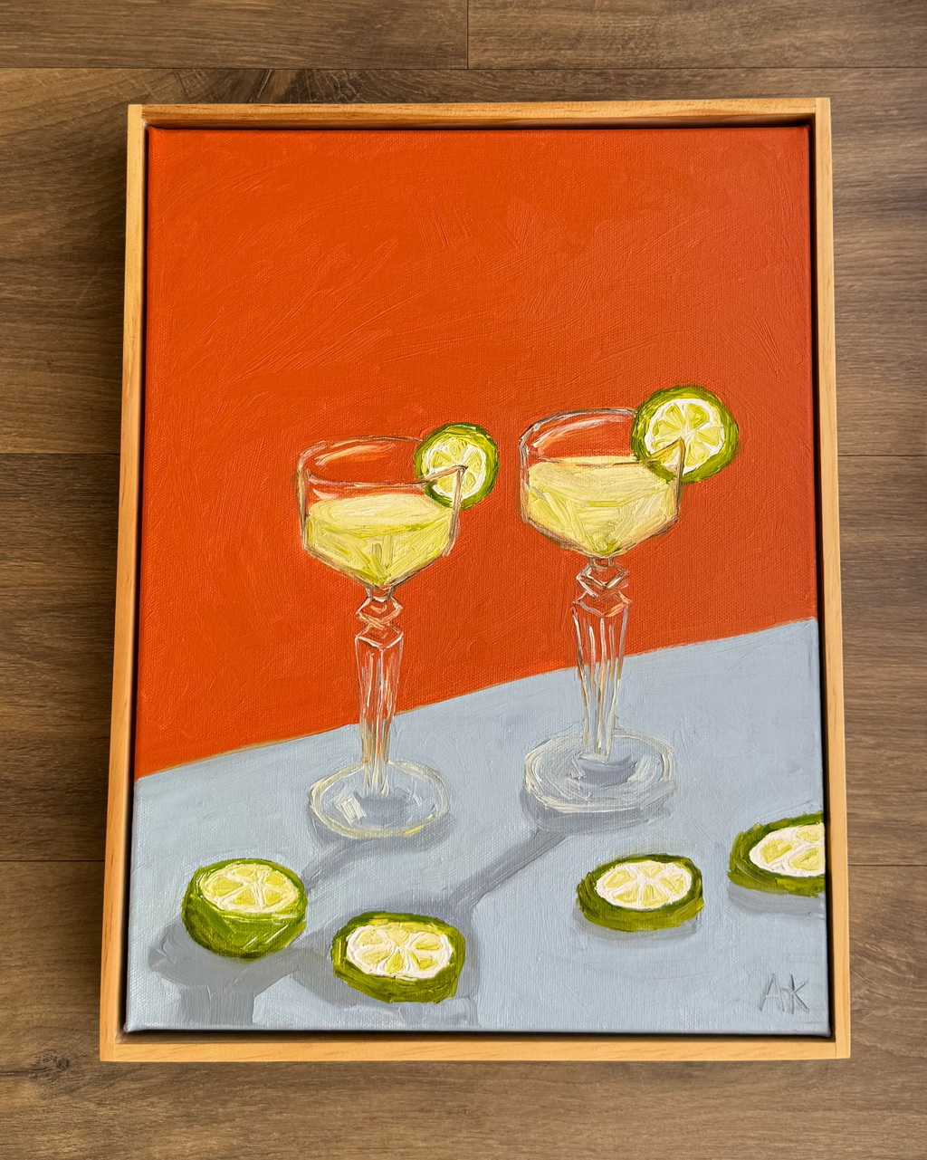 Framed artwork of two cocktail glasses with lime slices on a wooden surface.