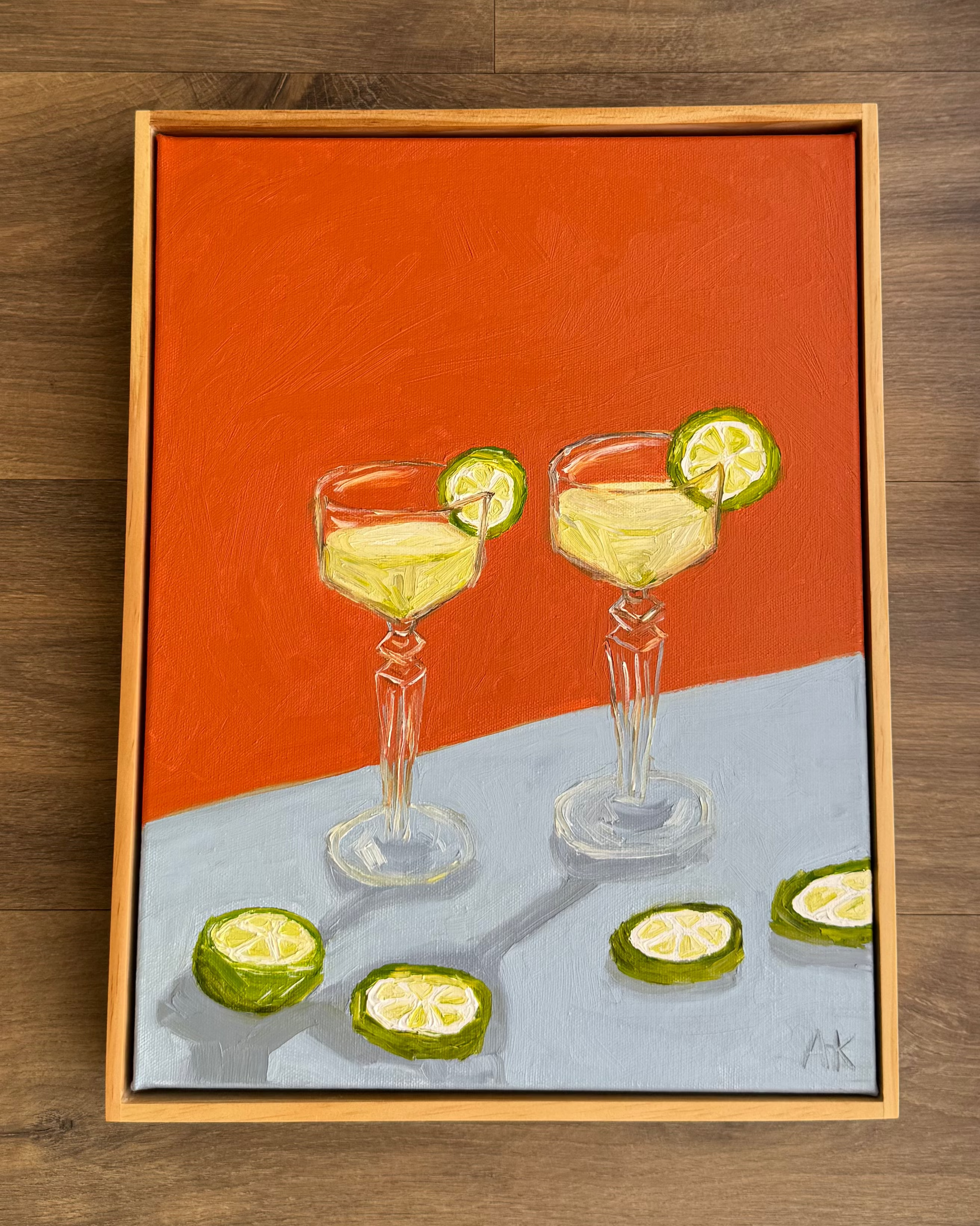 Framed artwork of two cocktail glasses with lime slices on a wooden surface.